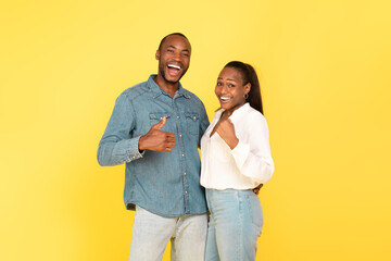 Joyful Black Couple Gesturing Thumbs Up And Yes, Yellow Background