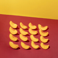 Creative pattern made with fresh peaches slice on dark red and yellow background. Minimal summer fruit arrangement.