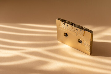 Gold fancy retro old audio cassette tape on beige color background. Retro mixtape, 1980s pop songs...