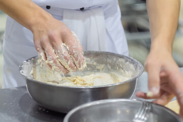 Baker, chef hands kneading fresh dough in steel bowl on kitchen table at cuisine of restaurant. Professional cooking, preparation, gastronomy and food concept