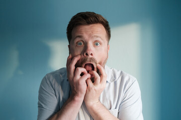 European man with a frightened, anxious expression stands against a blue background.