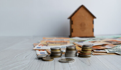 A toy house, stacks of coins and banknotes lie on the table. Concept of money market, financial economy and real estate insurance.