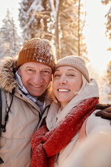 Vertical POV of happy senior couple taking selfie photo while enjoying hike in winter forest