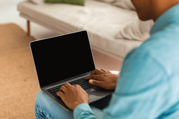Fototapeta premium Young black guy in jeans typing on laptop with blank screen, chatting remotely in social networks