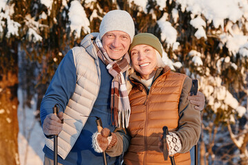 Waist up portrait of happy senior couple looking at camera while hiking in winter forest together
