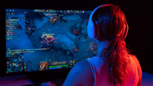 Rear view of a caucasian woman playing a computer game in neon light in the dark. - Powered by Adobe