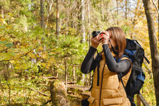 Young Caucasian Woman Hiker Taking Photos with Retro Film Camera in Autumn Forest