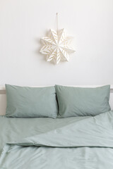 Christmas home decor. Winter bedroom decor. New year interior decorations. White paper snowflake on wall and bed with green linen.