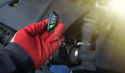 The master's hand holds a car alarm keychain. Installing an immobilizer in the car. Car security system. Keychain with buttons for the car.Sale of alarm systems for personal cars. - obrazy, fototapety, plakaty