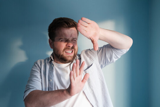 European man is annoyed by the sunlight, which blinds him. Blue background.