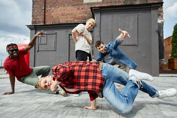Motion shot of young man doing handstand poses outdoors with all male breakdance team in background