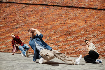 Portrait of all male breakdance team posing against brick wall outdoors in sunlight