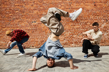 Portrait of all male breakdance team doing head stand against brick wall outdoors in sunlight