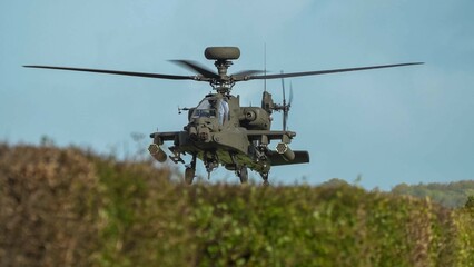 Fototapeta na wymiar close-up head-on view of ZM707 British army Boeing Apache Attack helicopter (AH-64E ArmyAir606) sitting low behind hedgerow