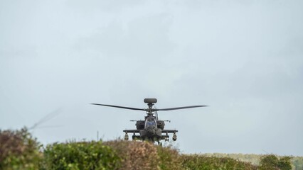 Fototapeta na wymiar close-up head on view of ZM707 British army Boeing Apache Attack helicopter (AH-64E ArmyAir606) hovering very low behind hedgerow