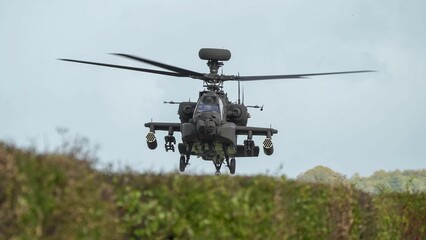 Fototapeta na wymiar close-up head on view of ZM707 British army Boeing Apache Attack helicopter gunship (AH64E AH-64E ArmyAir606) hovering low behind hedgerow