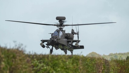 close-up head on view of ZM707 British army Boeing Apache Attack helicopter (AH-64E ArmyAir606) hovering low behind hedgerow