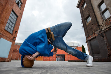 Full length shot of young man doing breakdance pose in urban factory setting outdoors and hiding face