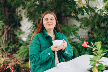 Portrait of beautiful woman drinking a cup of tea in cafeteria. Young caucasian Redhead woman in a cafe drinking coffee, happy emotions.