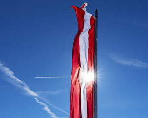 Bright red-white-red flag of austria against a clear sky on a sunny day
