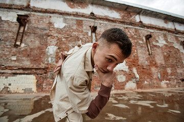 Fisheye shot of young man wearing streetstyle fashion and looking at camera in shabby urban setting with brick walls