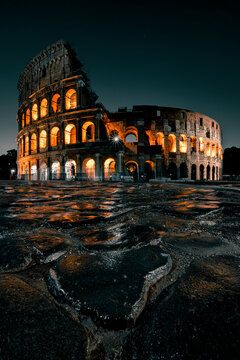 Portrait picture of the Roman Colosseum at night with wet cobblestones reflecting the illuminated ancient arena