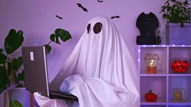 The ghost of Halloween uses a laptop to surf the Internet, to browse online stores, markets. A ghost makes an order computer for Halloween. The ghost pays for an online purchase. Neon light.