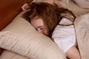 A young girl is fast asleep lying on her stomach with her face in a pillow down in bed at home
