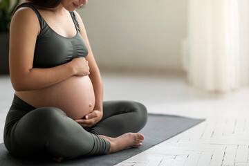 Young Pregnant Woman In Activewear Sitting On Yoga Mat And Embracing Belly