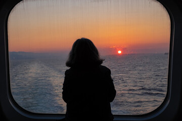 Thinking woman looking on the sea from ferry boat window during early morning sunrise - Powered by Adobe