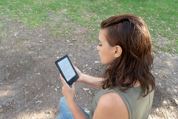 Young woman reading an e-book in the park. Copy space