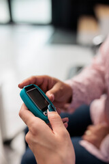 Close up of assistant doing insulin level measurement with instrument to help woman with diabetes, using glucometer to check glucose and sugar from blood. Patient attending checkup appointment.