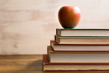 Shiny red apple sitting atop a stock of colorful books in front of a white textured background with room for copy
