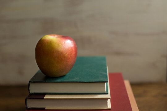 Shiny apple with colorful books against textured white background with room for text