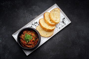 Baked eggplant caviar and vegetables with toast on a dark background