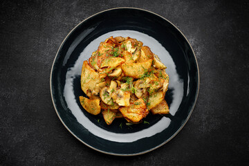 Fried potatoes with mushrooms on a dark background