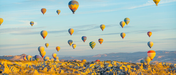 Wide panoramic shot. Plenty of colourful patterned hot-air balloons flying over beautiful and...