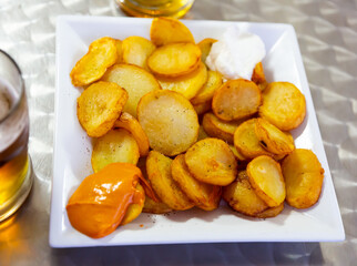 Delicious baked in oven yellow spicy potatoes bravas served at plate in cafe