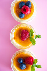 Top view of creme brulee dessert with baked sugar and fresh berries in bright sunshine on pink background.