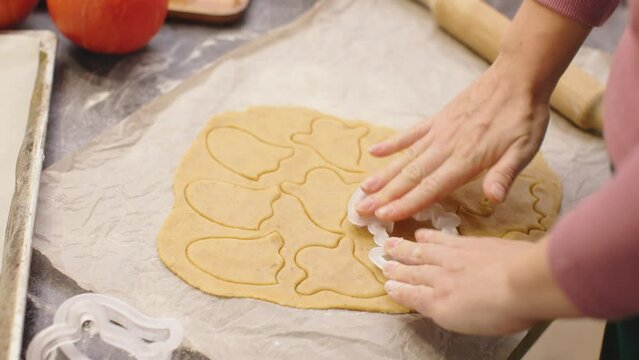 woman cutting cookies from handmade dough with pastry cutter pumpkin biscuits baking home kitchen autumn seasonal decoration. happy halloween party preparation sweet food biscuits scary monster ghost