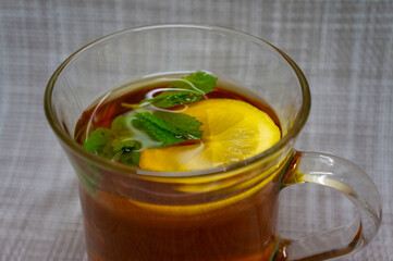 Transparent cup with black tea, lemon and mint, aesthetically warm photo.