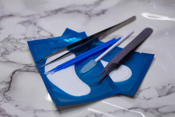 Set of eyelash extension tools with patches on a light marble background