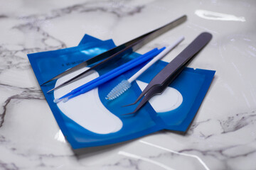 Set of eyelash extension tools with patches on a light marble background
