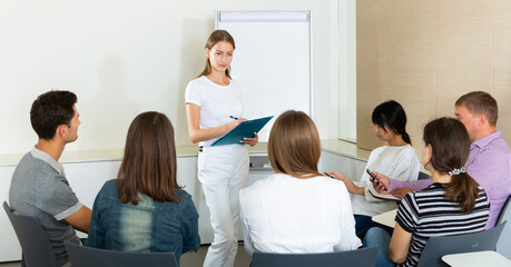 Positive young female business coach communicating with adult auditorium during training in office