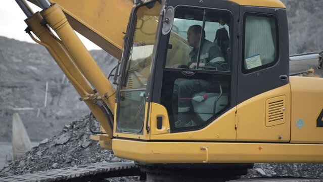 An excavator works at a gold mining site. The excavator cabin and the operator in it are shown.