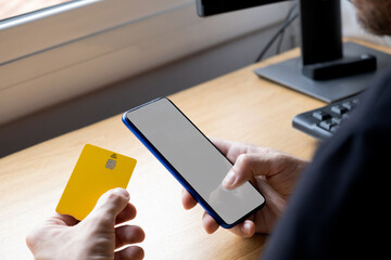 unrecognizable person holding a phone with a blank screen and a yellow credit card in his hand
