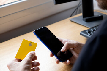 hand holding phone with blank screen, yellow credit card on the table.
