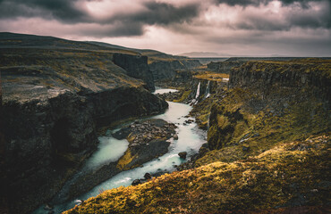 river flows through vally with waterfall, plants and dark clouds