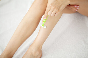 Young woman removing hair on legs with razor at bathroom