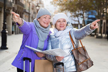 Fototapeta na wymiar Happy mature ladies travellers with suitcases visiting sights of European city with map